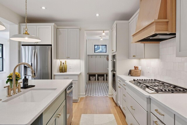 kitchen featuring a sink, custom exhaust hood, light countertops, decorative light fixtures, and appliances with stainless steel finishes