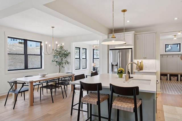 kitchen with a sink, plenty of natural light, a kitchen island with sink, stainless steel fridge, and light countertops