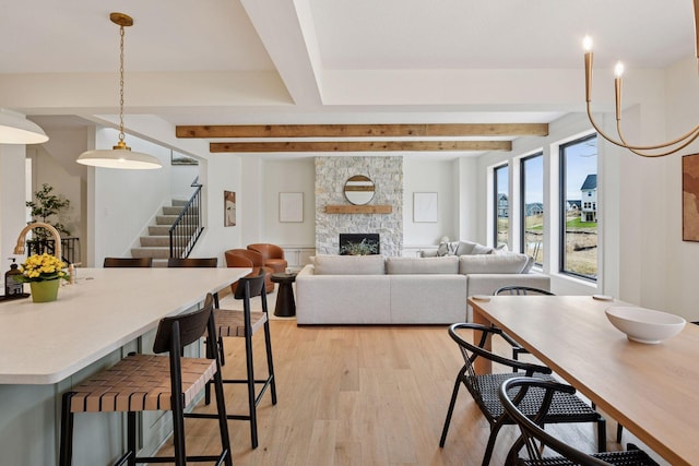 dining area featuring beam ceiling, stairs, light wood finished floors, and a fireplace
