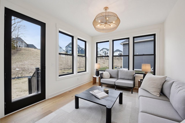 living area with an inviting chandelier, light wood-style floors, visible vents, and baseboards