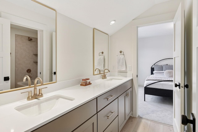 ensuite bathroom featuring lofted ceiling, wood finished floors, a sink, and double vanity
