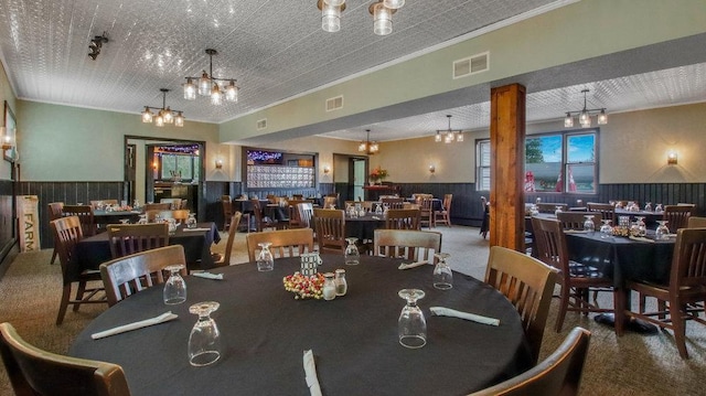 carpeted dining room featuring crown molding, a wainscoted wall, a chandelier, and visible vents