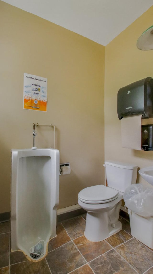 half bathroom with baseboards, stone finish floor, and toilet