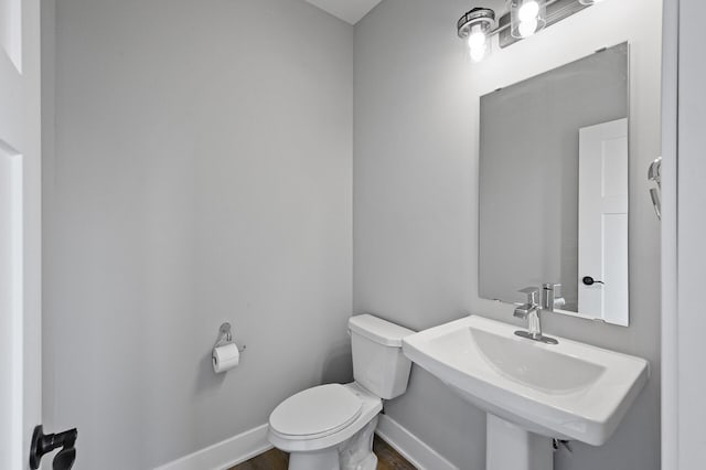 bathroom featuring wood finished floors, toilet, baseboards, and a sink