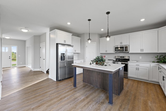 kitchen with light countertops, wood finished floors, a center island, appliances with stainless steel finishes, and white cabinetry