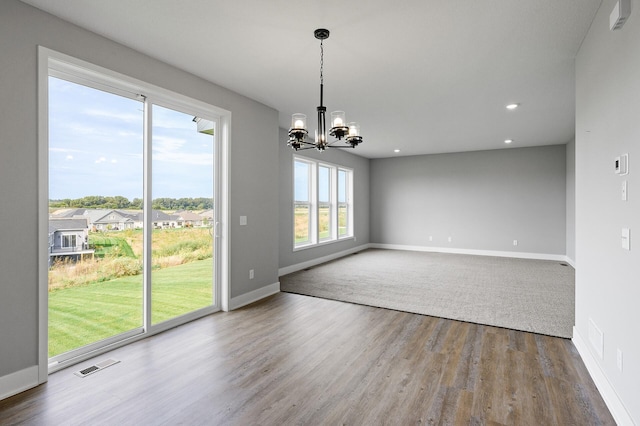 unfurnished dining area with baseboards, wood finished floors, visible vents, and an inviting chandelier