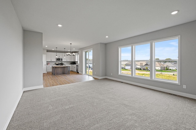 unfurnished living room with light carpet, visible vents, baseboards, recessed lighting, and a chandelier