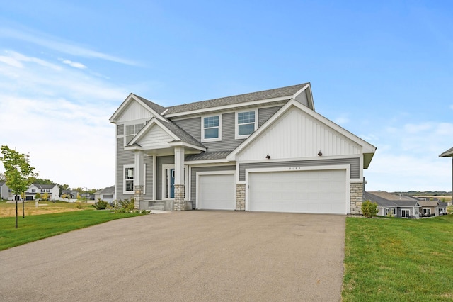 craftsman-style home with a front lawn, driveway, stone siding, and roof with shingles