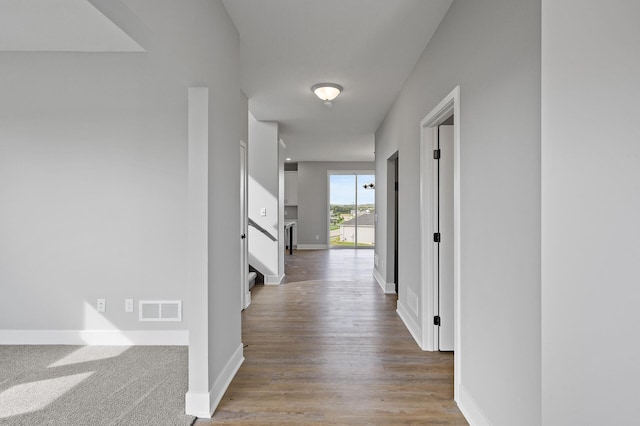 hallway featuring wood finished floors, visible vents, and baseboards