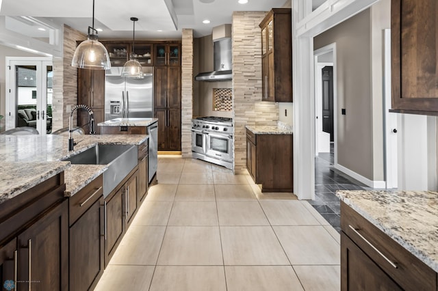kitchen with stainless steel appliances, wall chimney range hood, a sink, tasteful backsplash, and glass insert cabinets