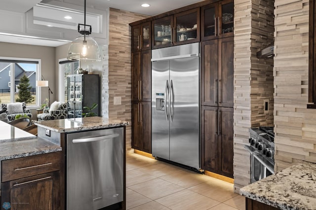 kitchen with stainless steel appliances, light tile patterned floors, light stone countertops, dark brown cabinetry, and hanging light fixtures