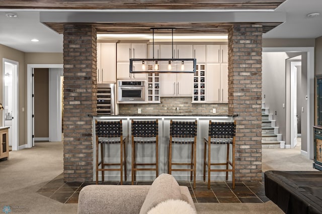 kitchen with dark carpet, stainless steel oven, ornate columns, a breakfast bar, and dark countertops