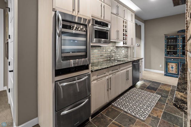 kitchen with a sink, dishwasher, baseboards, backsplash, and stone tile floors