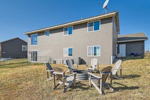 rear view of property featuring a fire pit, a yard, and fence