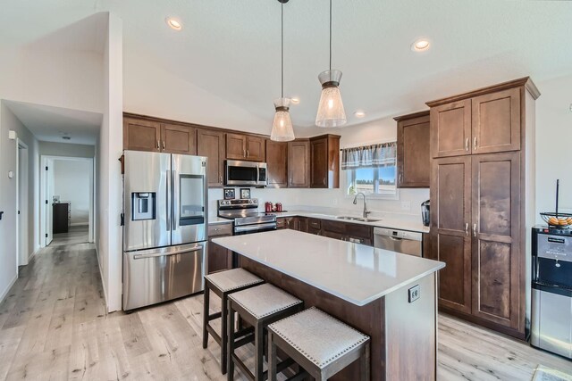 kitchen with a sink, light wood-style floors, stainless steel appliances, light countertops, and a kitchen island