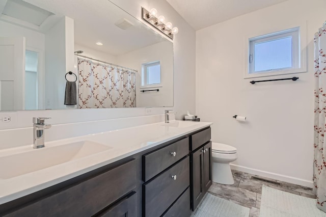 bathroom featuring toilet, a sink, double vanity, and baseboards