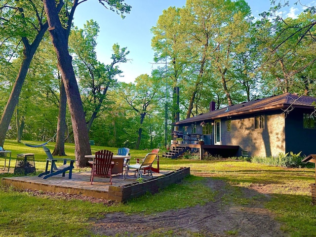 view of green lawn with a deck and a fire pit