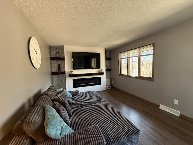 living area with wood finished floors, a textured ceiling, and a glass covered fireplace