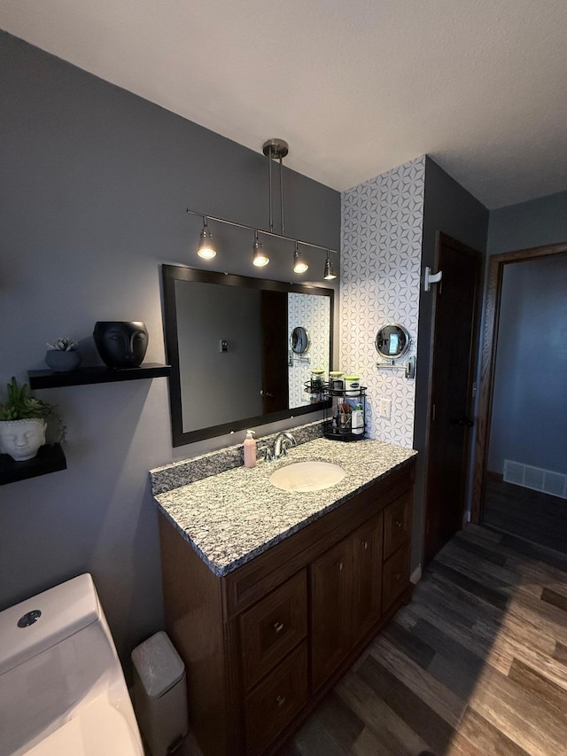 bathroom with toilet, wood finished floors, rail lighting, and vanity