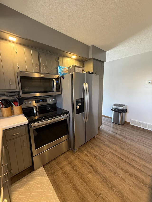 kitchen with appliances with stainless steel finishes, light wood-style flooring, a textured ceiling, gray cabinetry, and light countertops