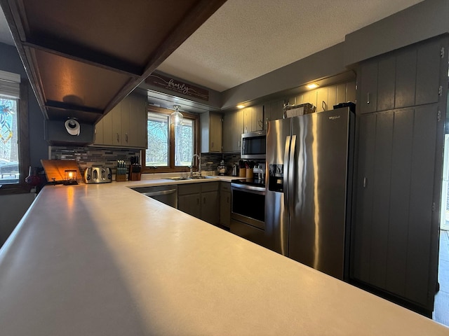 kitchen with appliances with stainless steel finishes, decorative backsplash, a sink, light countertops, and a textured ceiling