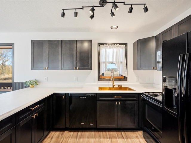 kitchen featuring black appliances, a sink, light wood-style flooring, light countertops, and dark cabinetry