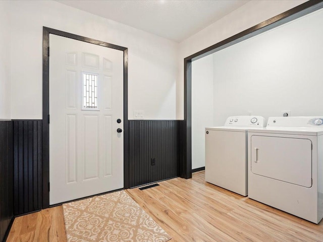 laundry room with separate washer and dryer, light wood-style floors, and wainscoting