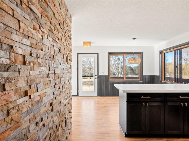 kitchen featuring a wainscoted wall, dark cabinetry, light countertops, light wood-style flooring, and hanging light fixtures