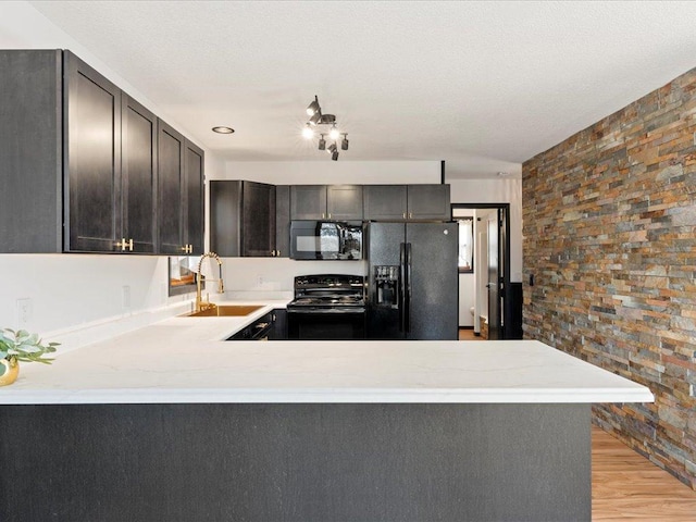 kitchen with black appliances, a sink, a peninsula, and light wood-type flooring
