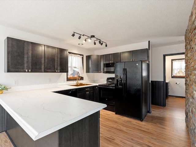 kitchen featuring black appliances, a sink, a peninsula, light wood finished floors, and a textured ceiling
