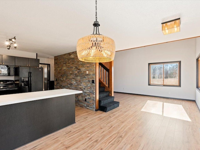 kitchen featuring black appliances, light wood-type flooring, decorative light fixtures, and light countertops