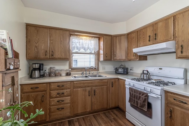 kitchen with brown cabinetry, under cabinet range hood, a sink, and white range with gas stovetop