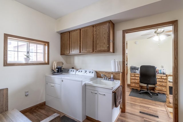 laundry room with cabinet space, independent washer and dryer, light wood-style floors, and a sink