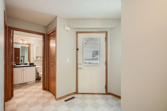 doorway to outside featuring light floors, baseboards, a textured ceiling, and a sink