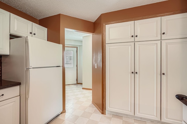 kitchen with freestanding refrigerator, light floors, a textured ceiling, white cabinetry, and dark countertops