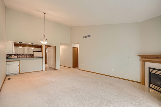 unfurnished living room featuring high vaulted ceiling, light colored carpet, a fireplace with flush hearth, and baseboards
