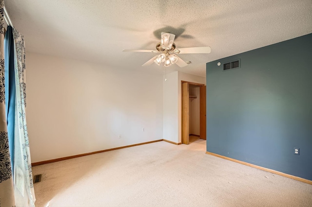 empty room with light colored carpet, ceiling fan, baseboards, and a textured ceiling