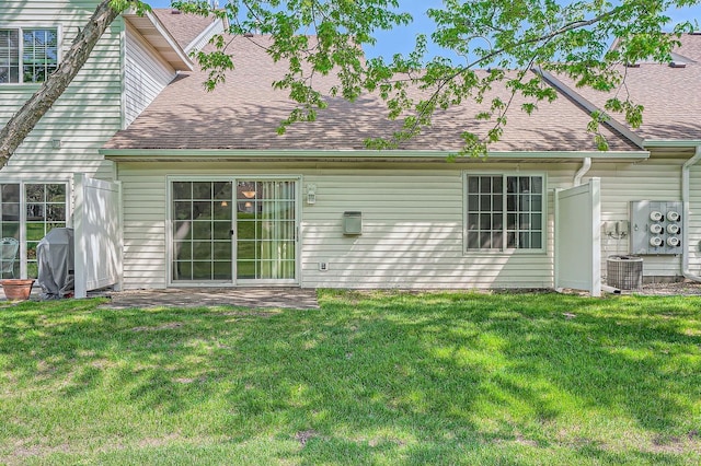 back of house featuring roof with shingles, central air condition unit, and a lawn