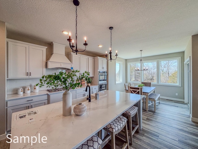 kitchen with a chandelier, custom range hood, dark wood finished floors, baseboards, and appliances with stainless steel finishes
