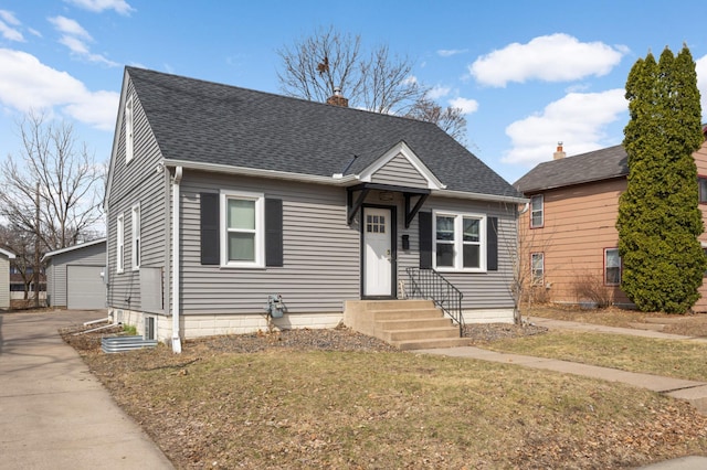 view of front of property featuring a garage, a chimney, a shingled roof, an outbuilding, and a front yard