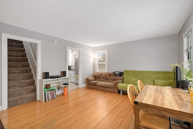 living area featuring light wood finished floors, a textured ceiling, and stairs