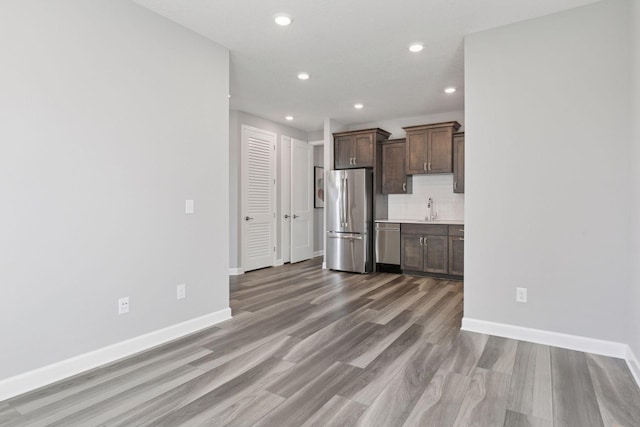 kitchen featuring appliances with stainless steel finishes, a sink, light wood-style floors, baseboards, and recessed lighting