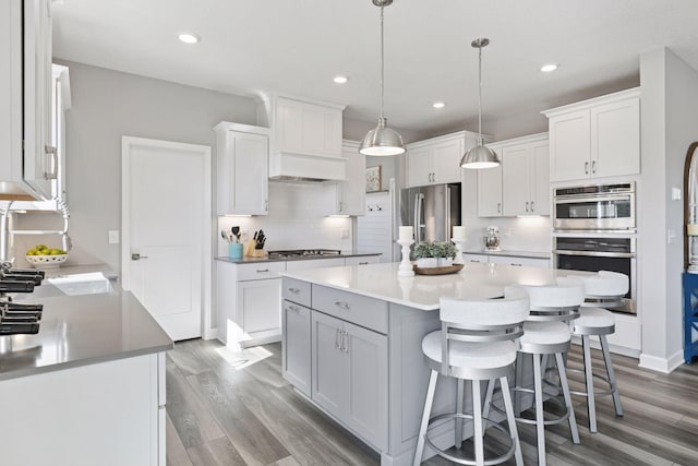 kitchen with light wood finished floors, stainless steel appliances, tasteful backsplash, white cabinetry, and a breakfast bar area