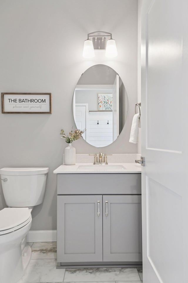 bathroom featuring marble finish flooring, vanity, toilet, and baseboards