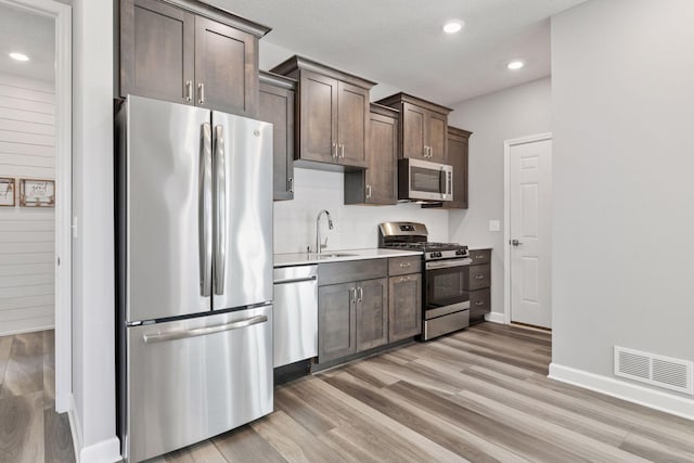 kitchen with stainless steel appliances, light wood-style flooring, dark brown cabinetry, light countertops, and recessed lighting