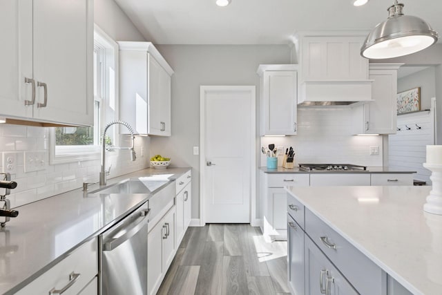 kitchen with stainless steel appliances, a sink, backsplash, white cabinets, and hanging light fixtures