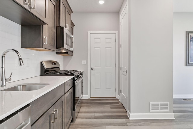 kitchen with appliances with stainless steel finishes, a sink, light wood finished floors, decorative backsplash, and dark brown cabinets