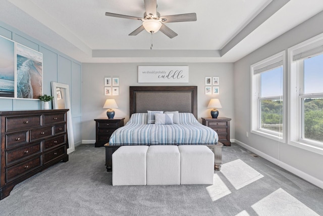 bedroom featuring a raised ceiling, carpet, baseboards, and a ceiling fan