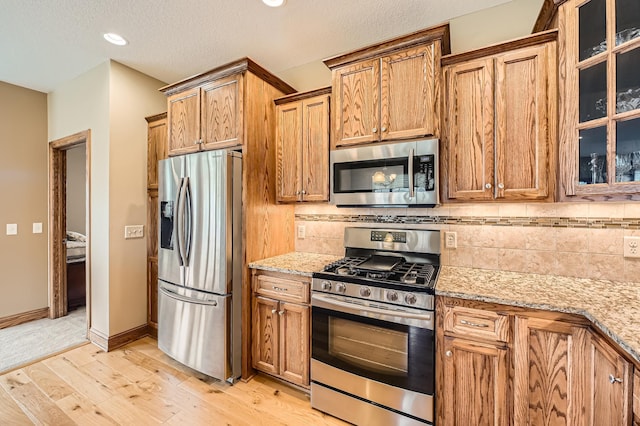 20620 Everton Way N, Forest Lake, MN 55025 - kitchen featuring appliances with stainless steel finishes, brown cabinets, light stone counters, backsplash, and light wood-style flooring