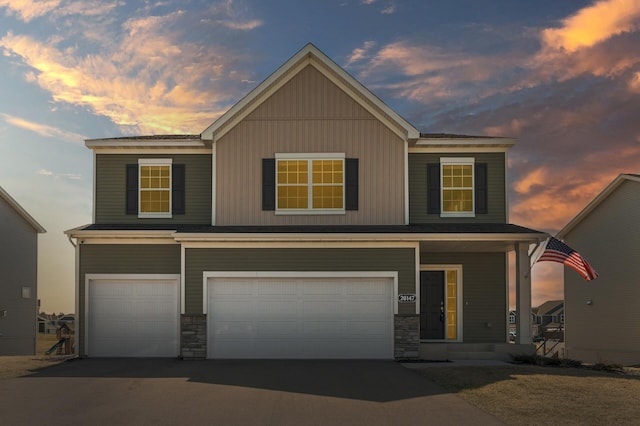 view of front of house featuring a garage, driveway, stone siding, and covered porch